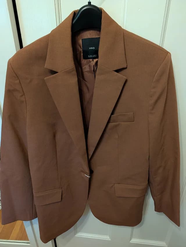 A chocolate brown blazer on a black hanger against a white door, as a phone photo
