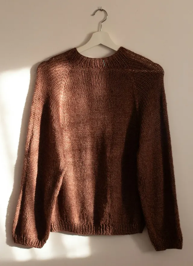 A brown knit sweater on a white hanger against a sunlit wall, as a phone photo